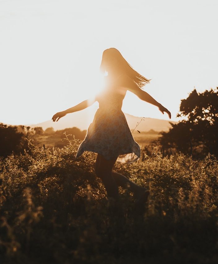 Girl dancing in a field while the sun in setting.