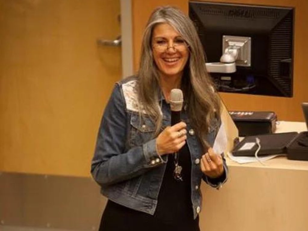 A woman in a jean jacket, with a microphone in her hand, smiling.